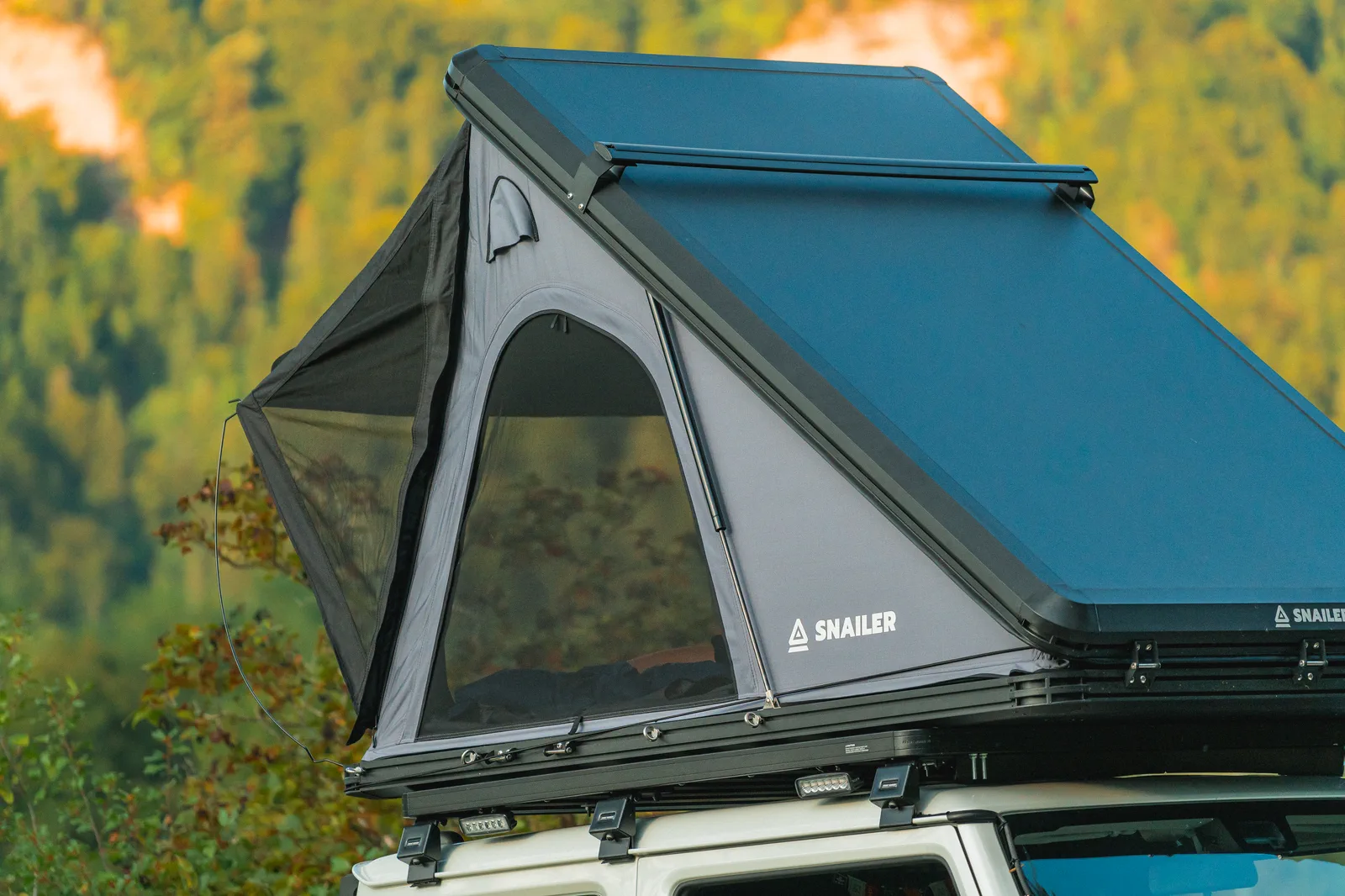 SNAILER hard-shell roof tent opened beside a forest